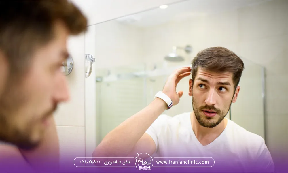 تصویر مربوط به یک آقاست که تیشرت سفید پوشیده و جلوی آینه به خودش نگاه می کنه و به موهاش دست می کشد